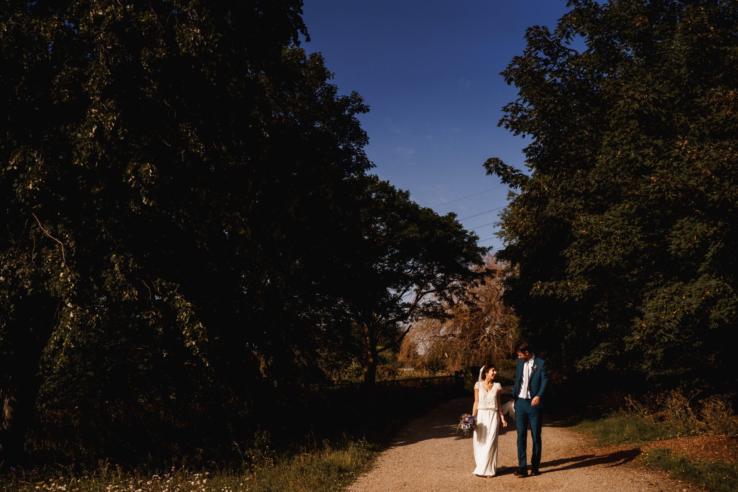 Wedding couple walking through Walthamstow Wetlands with a blue sky behind